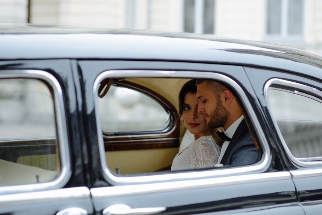 Beautiful happy young bride and groom looking from retro auto