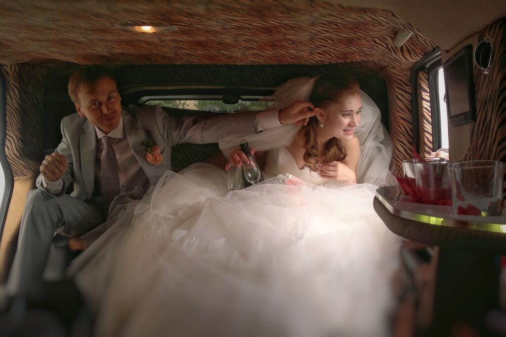 The newlyweds sit in a limousine and the husband pulls his wife by the ear from the window.
